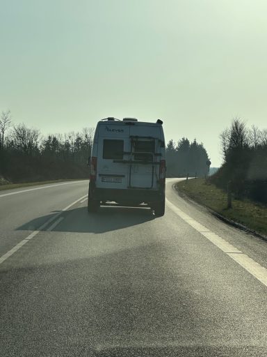 Weißer Campingbus auf einer kurvigen Landstraße bei sonnigem Wetter.