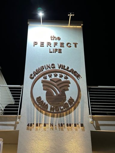 Schild mit der Aufschrift „the PERFECT LIFE - Camping Village“ bei Nacht.