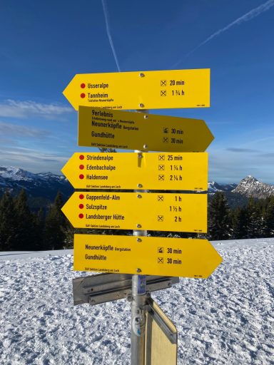 Gelbe Wegweiser mit Richtungen und Entfernungen zu verschiedenen Zielen in den Bergen.