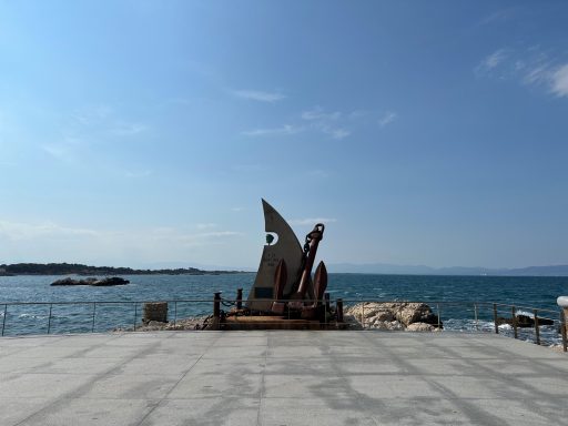 Bootsanleger mit einem großen Schiffsanker und Blick auf das Meer unter blauem Himmel.