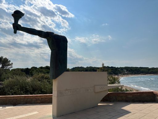 Skulptur eines menschlichen Beins, das aus einem Boot ragt, am Ufer.
