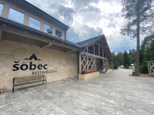 Eingang zum Hotel Šobec mit Holzverkleidung und benachbartem Gartenbereich.