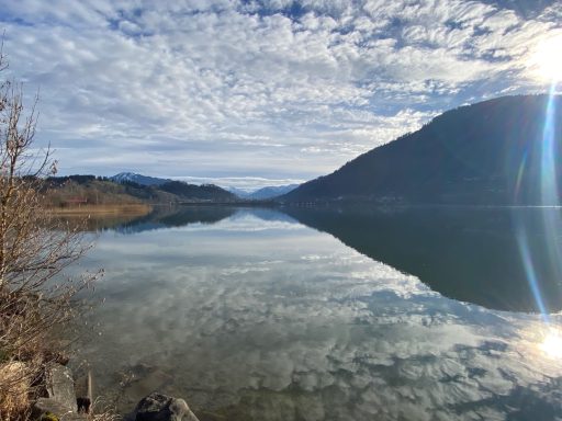 Ruhiger See mit Bergen im Hintergrund und bewölktem Himmel.