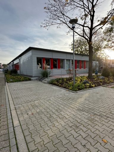 Einfamilienhaus mit roten Fenstern, vor einem Garten und einer gepflasterten Zufahrt.